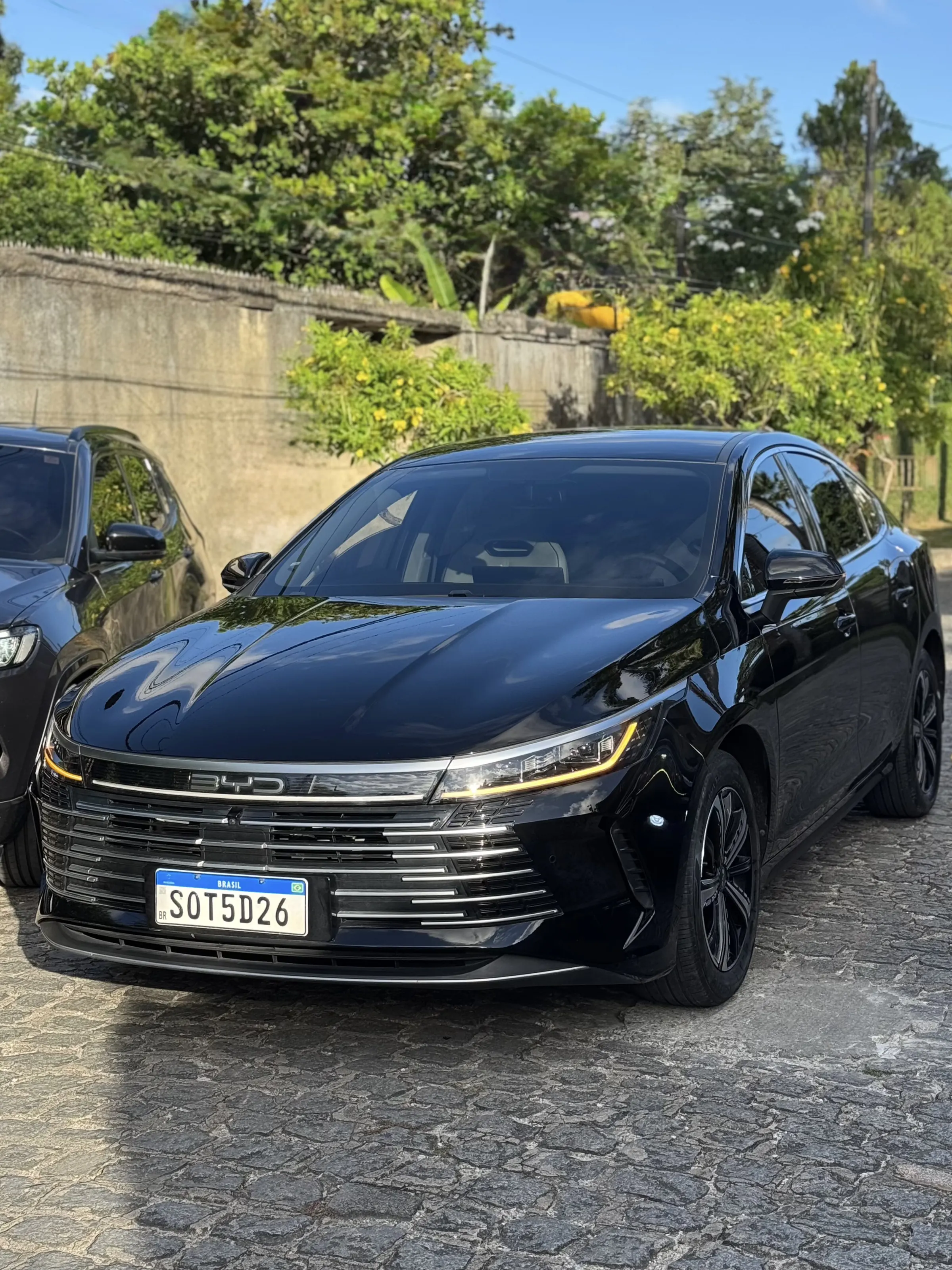 Sedan executivo preto da frota Jompu estacionado em rua arborizada no Recife