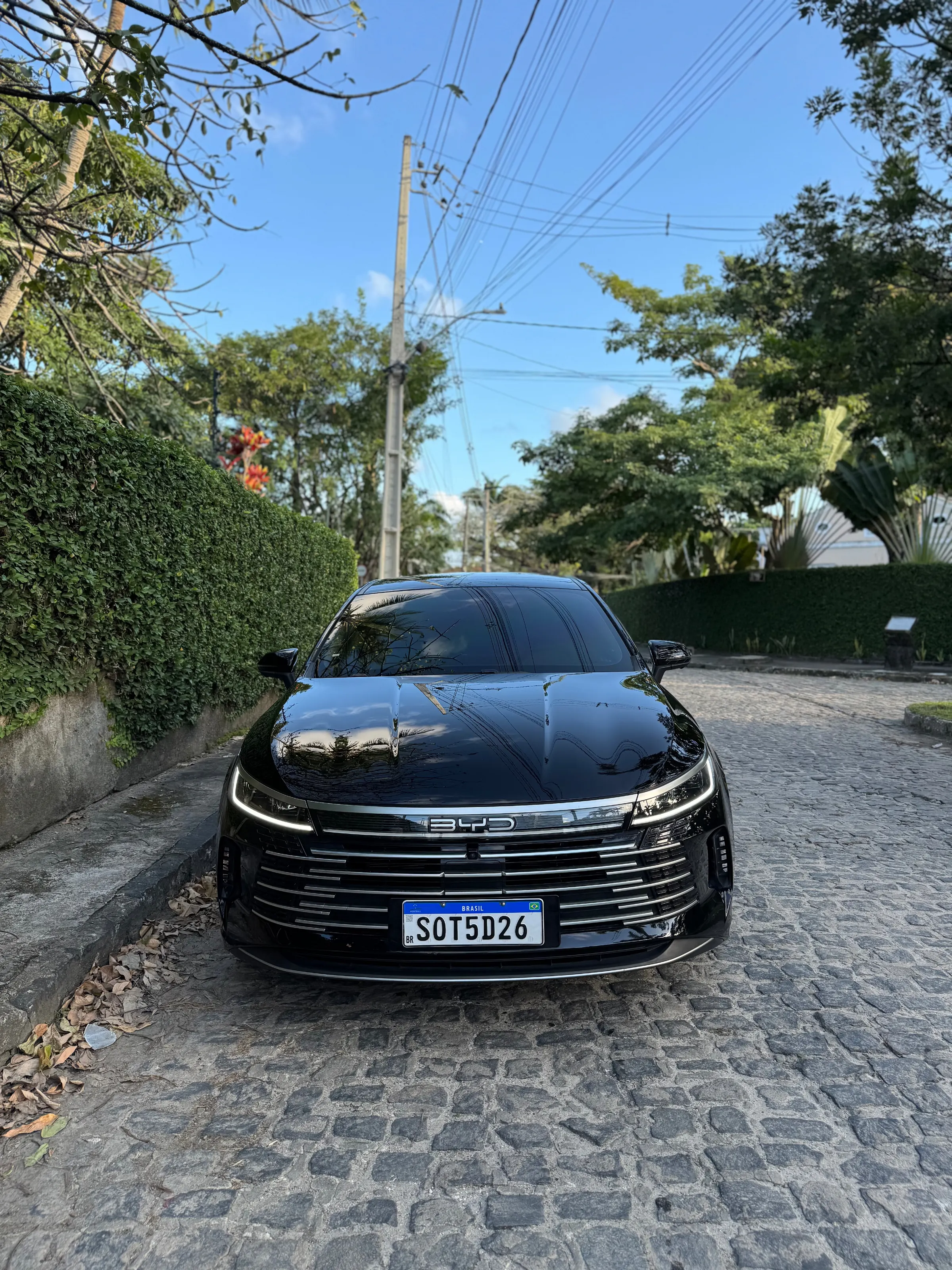 Sedan elétrico preto da frota Jompu visto de frente em rua de paralelepípedo